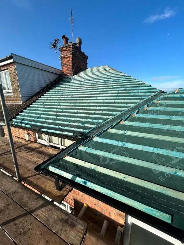 New breathable membrane laid across the rafters with fresh battens on top, the valley left open ahead of the leadwork, and the brick chimney stack rising behind.