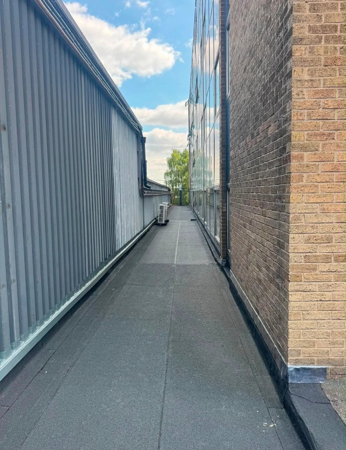 The walkway between the two buildings after the overlay, re-covered in clean mineral-finish felt with neat new upstands and flashings dressed against the brickwork.