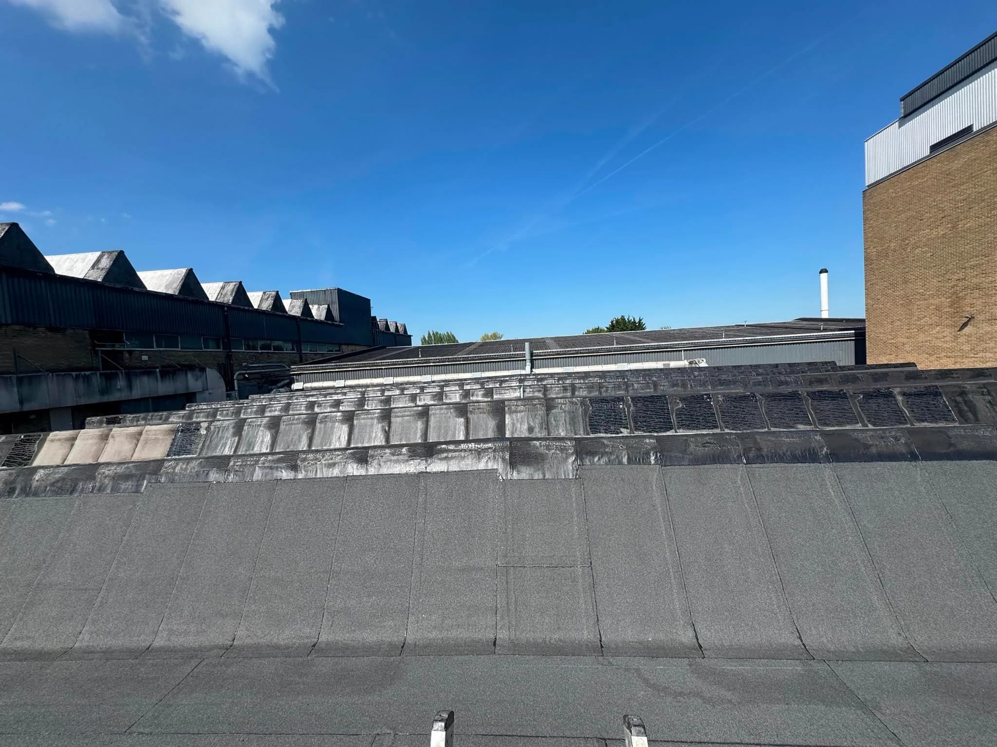 Mid-job on the main slopes: new mineral-surfaced sheets laid across the lower roof with the darker bitumen detailing still being worked along the ridges and upstands above.