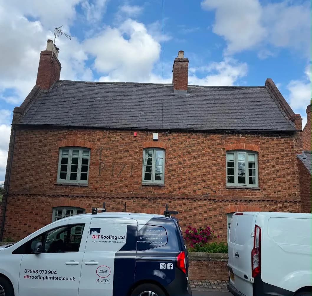 The listed house before work: a two-storey red-brick property with a dark, aged slate roof, two brick chimney stacks and pale green casement windows, with DLT Roofing's branded van parked on the road outside.