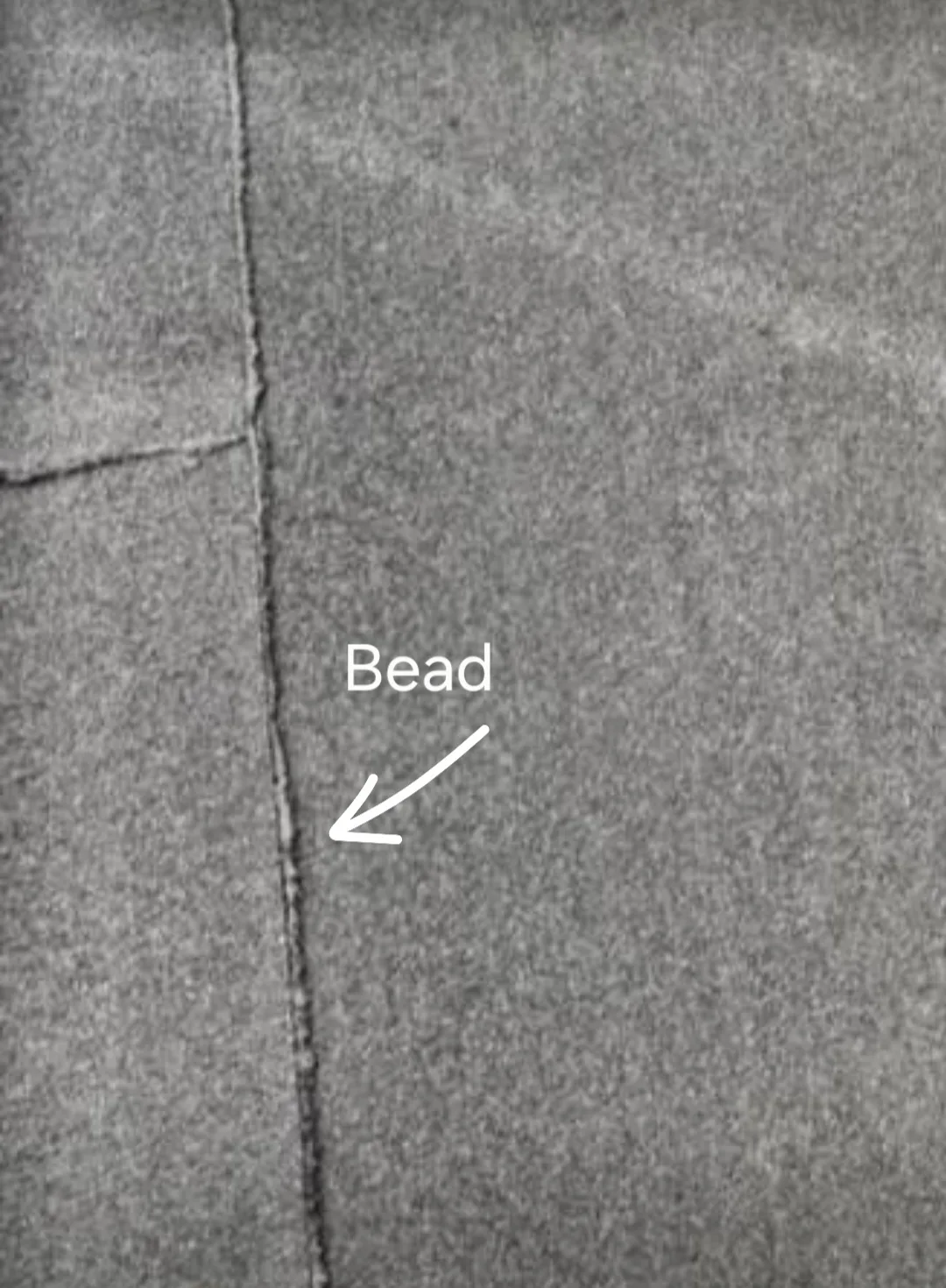 Close-up of a bitumen felt roof seam with an arrow and label marking the raised bitumen bead that has squeezed out along the join, showing what a continuous, properly sealed seam looks like.