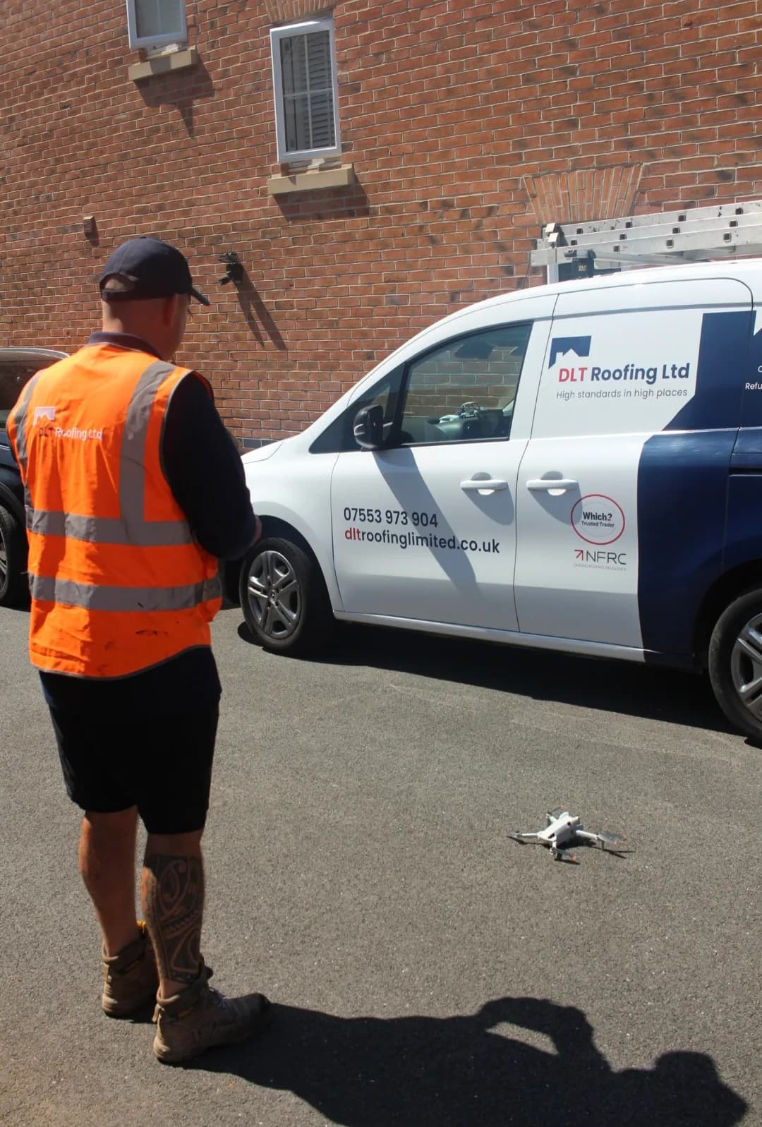 A survey drone sitting ready on the tarmac beside the DLT Roofing van, its livery showing the phone number, the Which? Trusted Trader mark and the NFRC mark, with a ladder racked on the roof and a surveyor in hi-vis standing alongside.