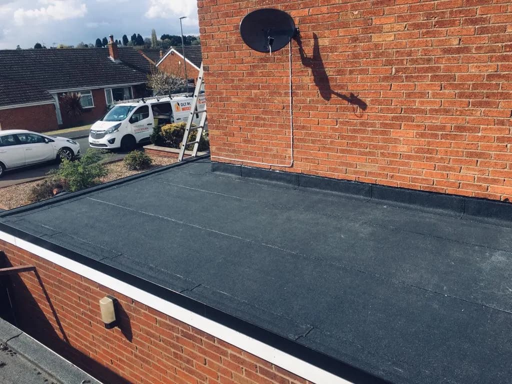 A finished dark felt flat roof on a domestic extension, with a branded DLT Roofing van parked on the driveway beyond.
